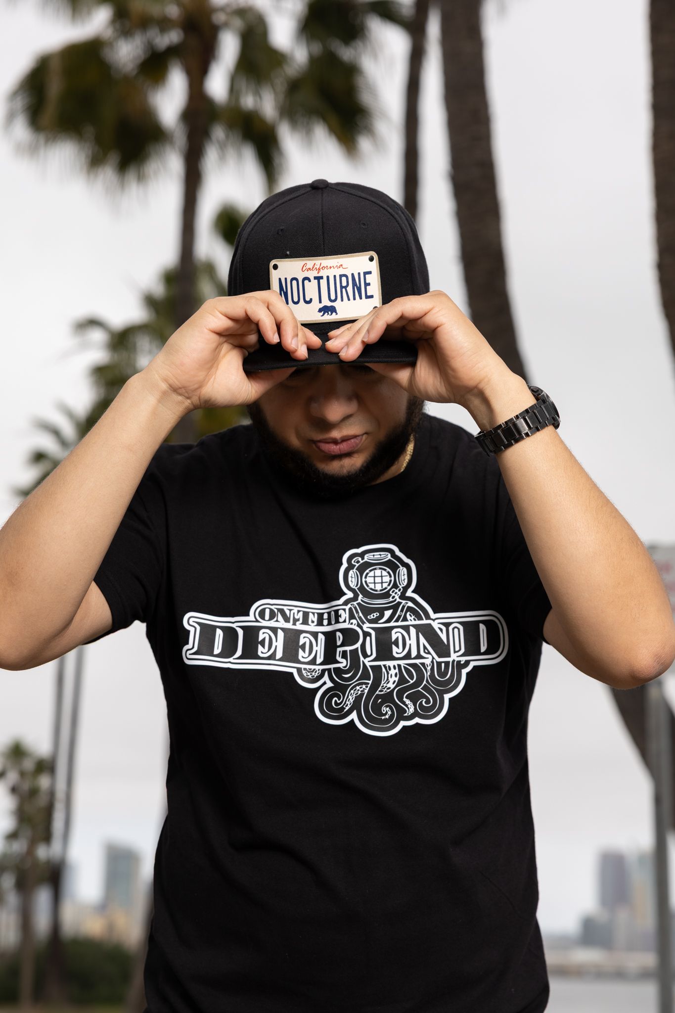 Person adjusting baseball cap while wearing black Defend branded t-shirt outdoors.