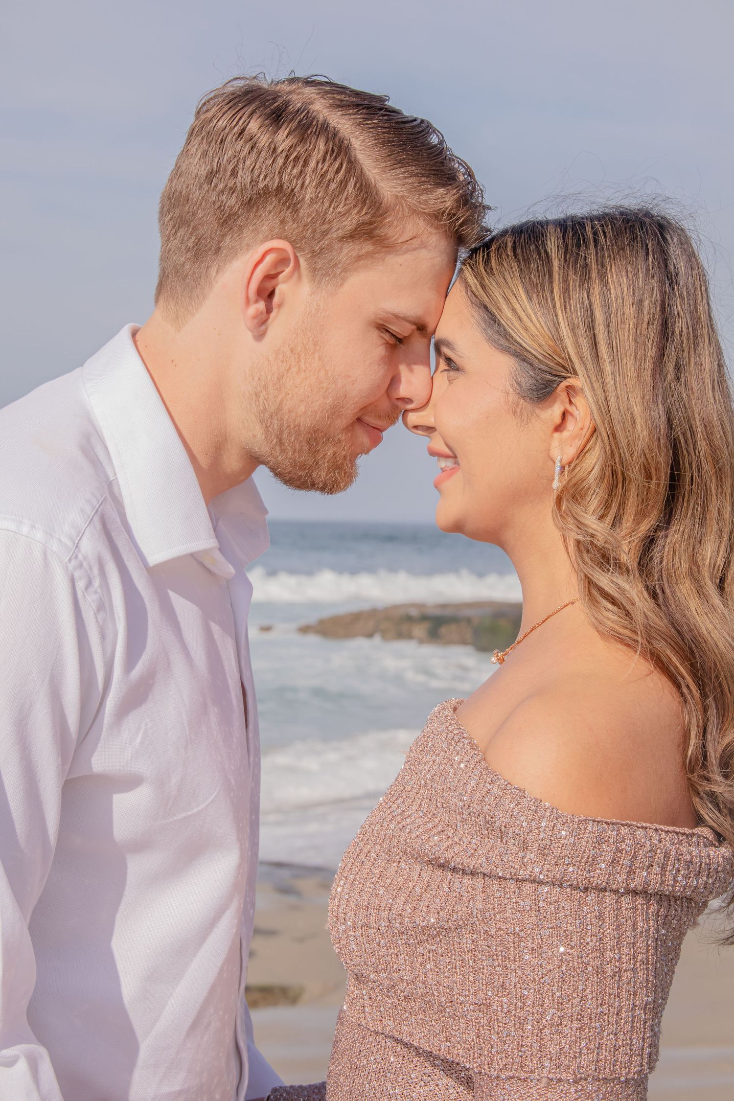 Romantic close-up of a couple sharing tender moments on a beach with ocean waves in background.