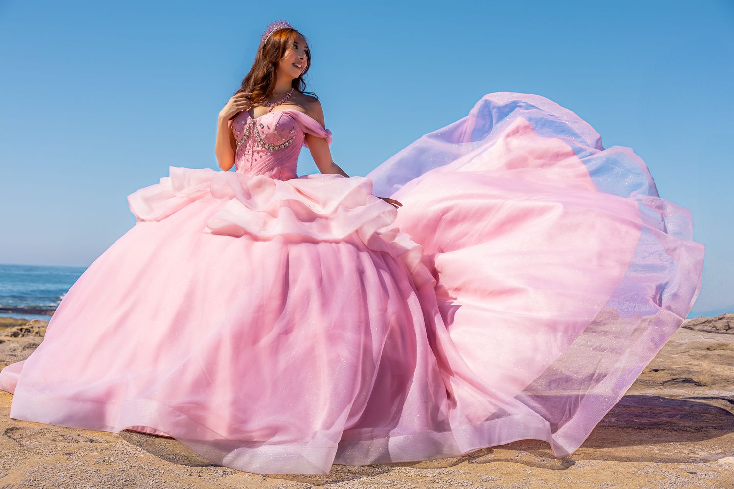 Flowing pink princess gown photographed against beach landscape at sunset.