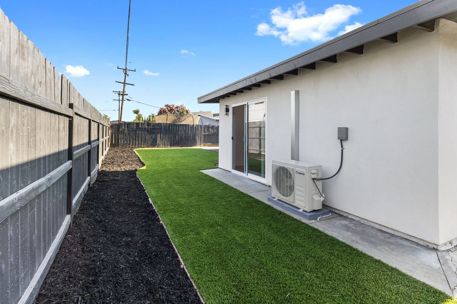 Side view of white house exterior with artificial turf and mulch landscaping.