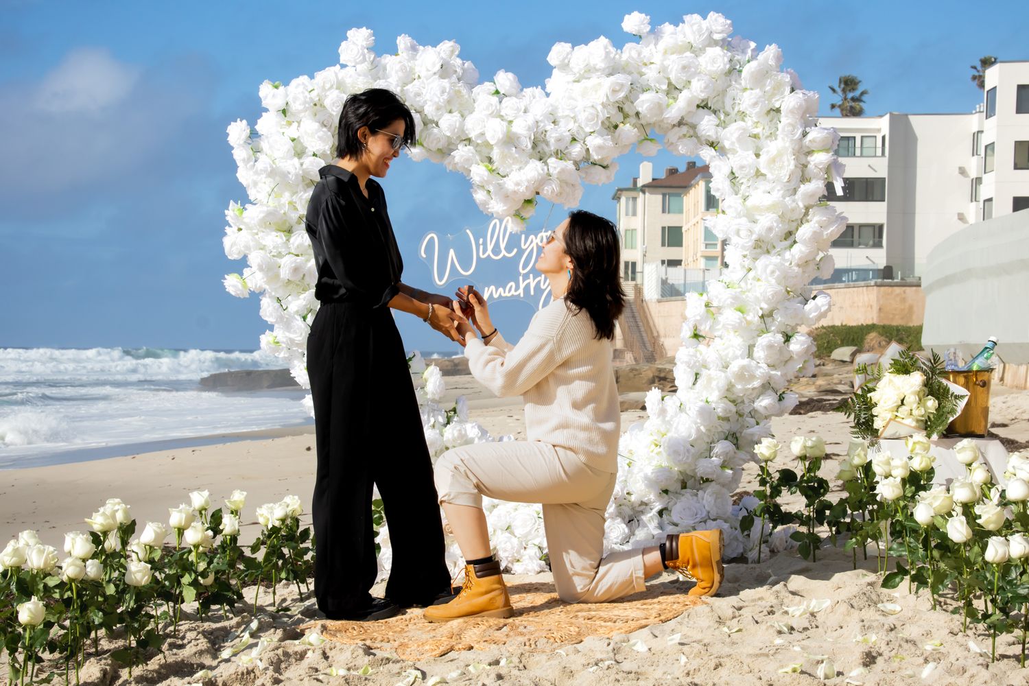 Beautiful outdoor proposal setting with white balloon arch and floral arrangements by the beach.