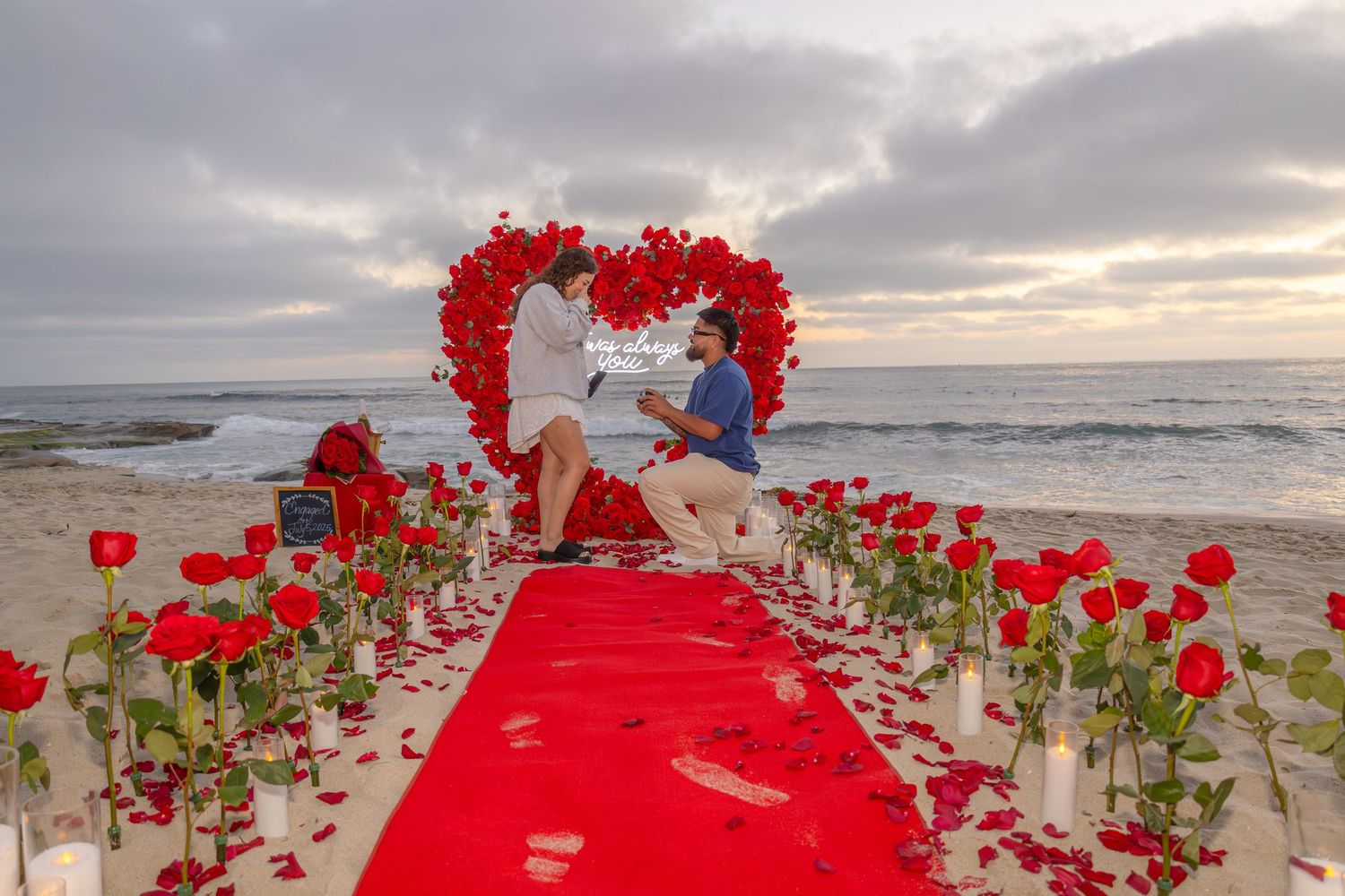 Heart-shaped walkway made of red roses on beach during sunset.