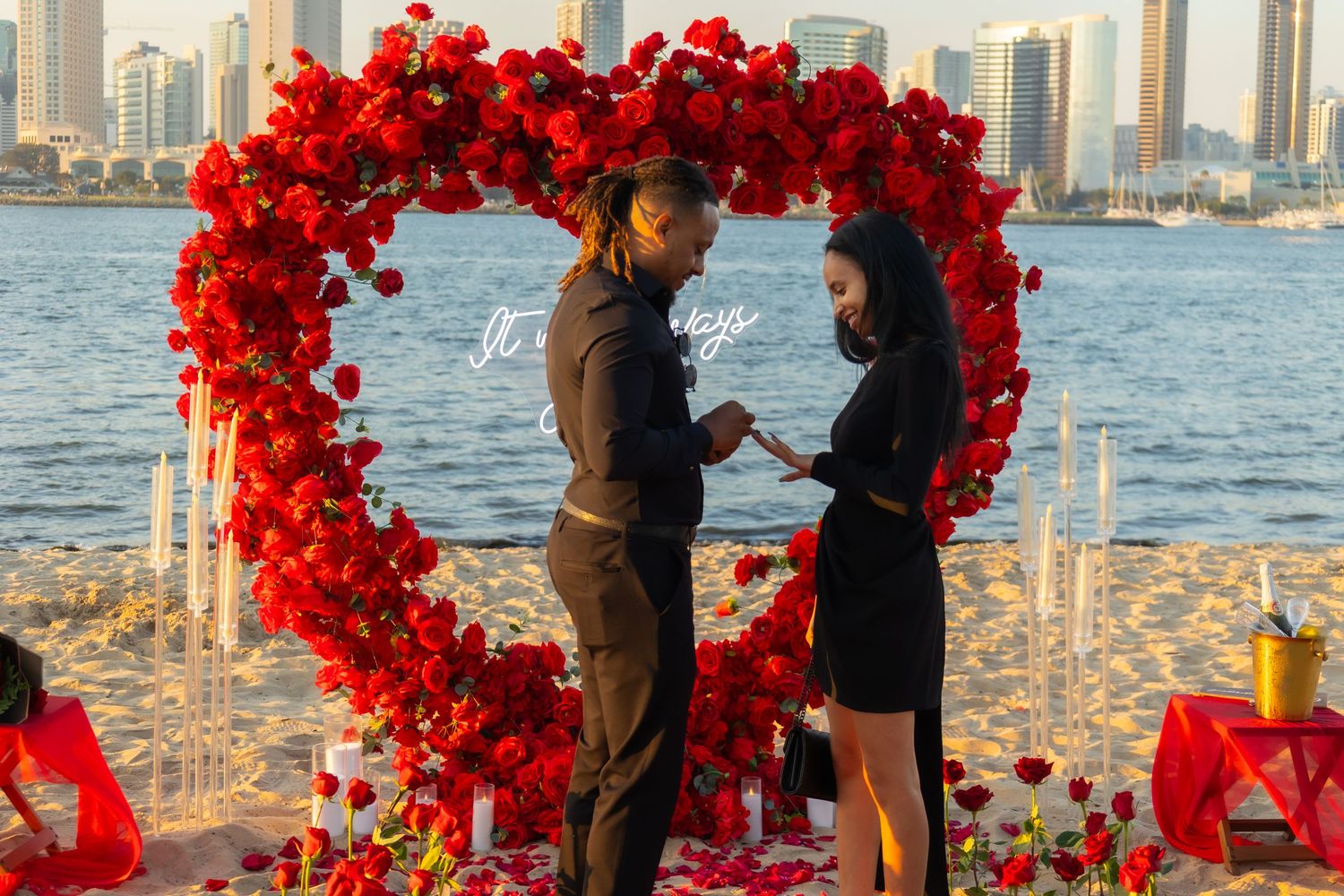 Red floral arch with city skyline backdrop during sunset proposal.