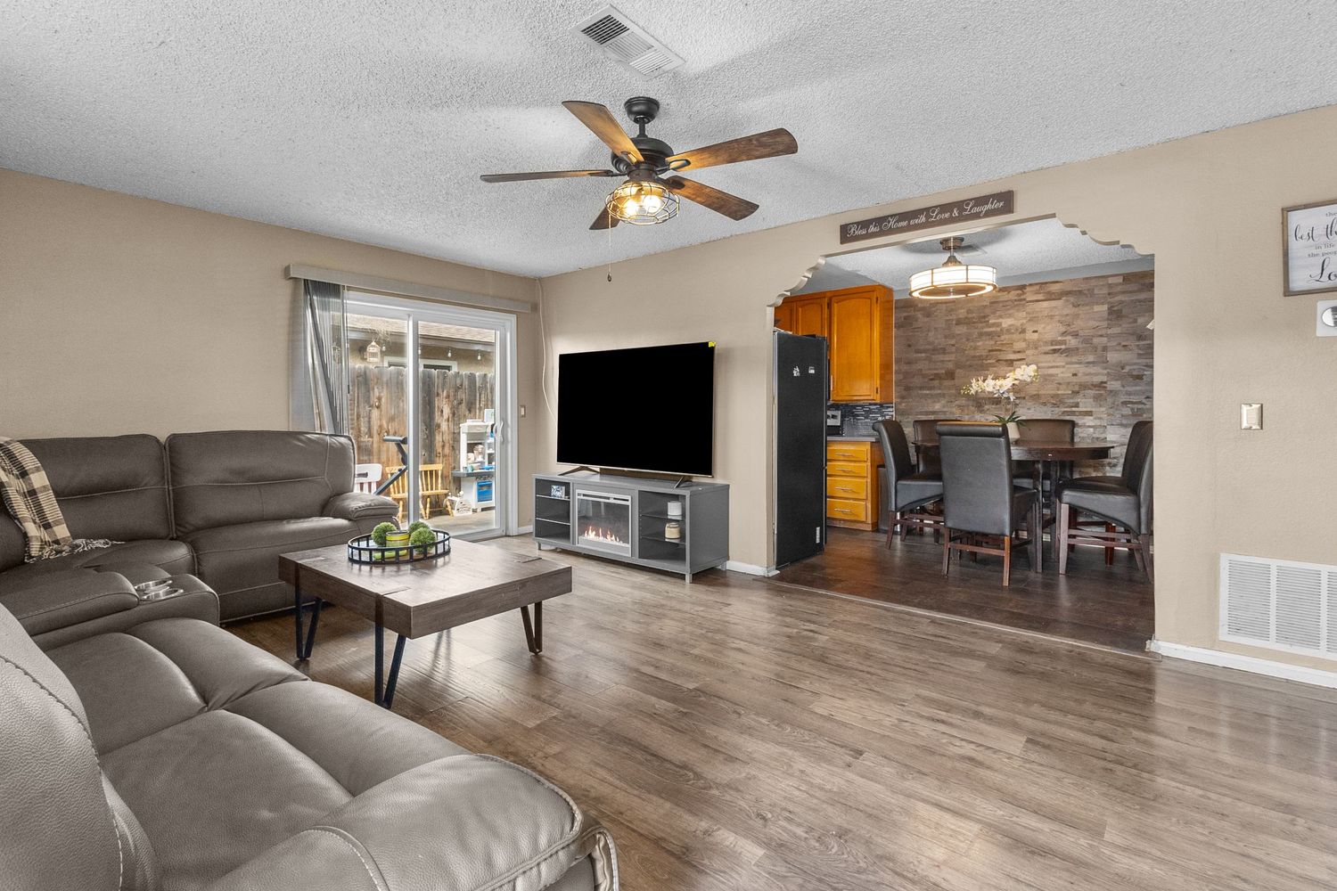 Spacious living room with beige walls, ceiling fan, and wood-look flooring.