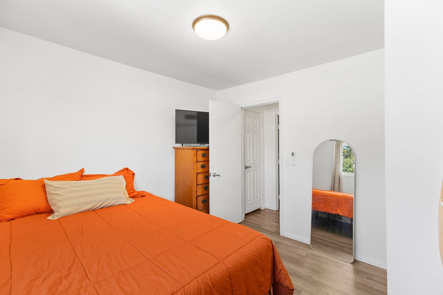 Bright bedroom with orange bedding, white walls, and hardwood flooring.