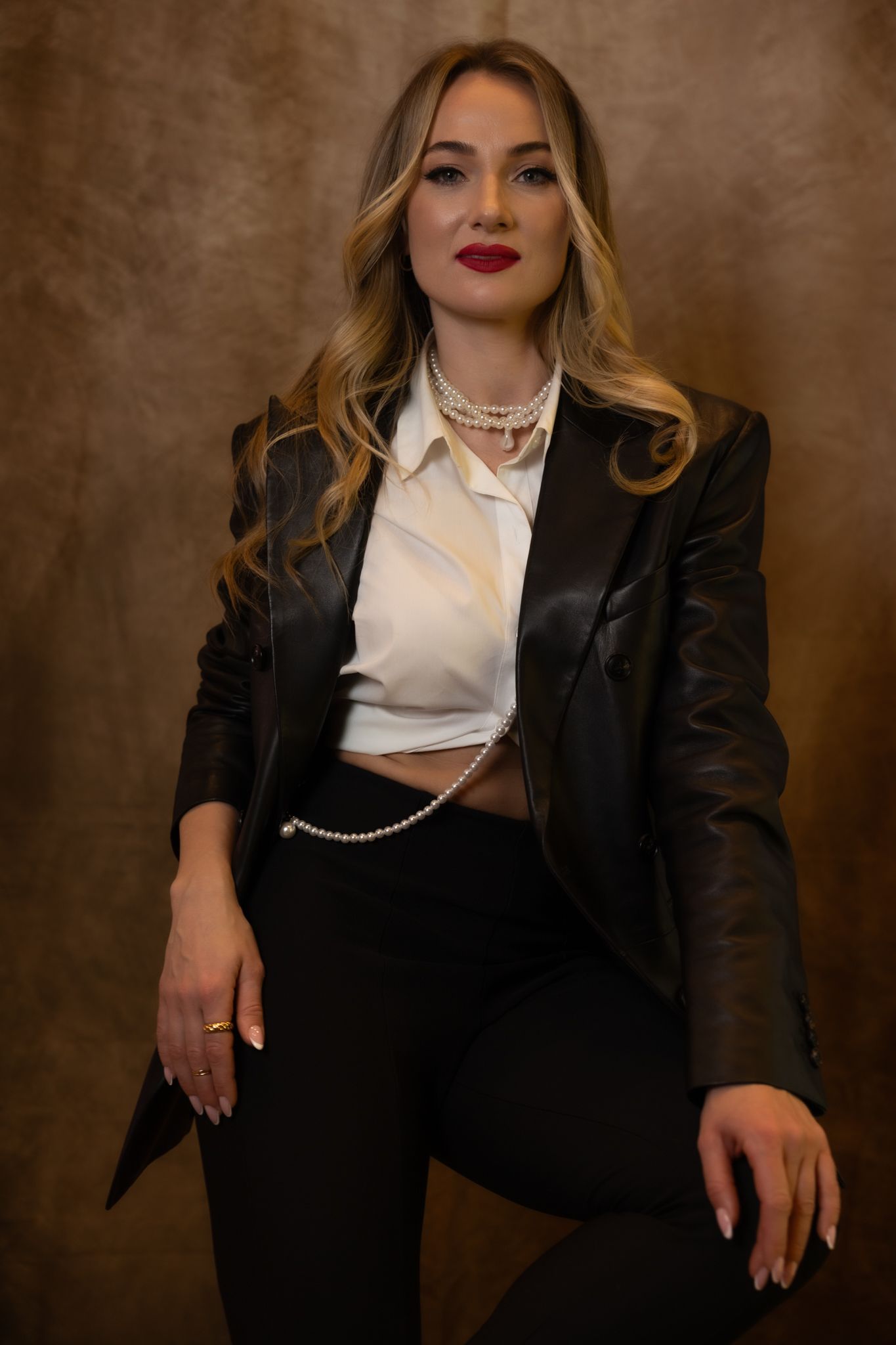 Stylish fashion portrait in black blazer with pearl necklace against brown backdrop.