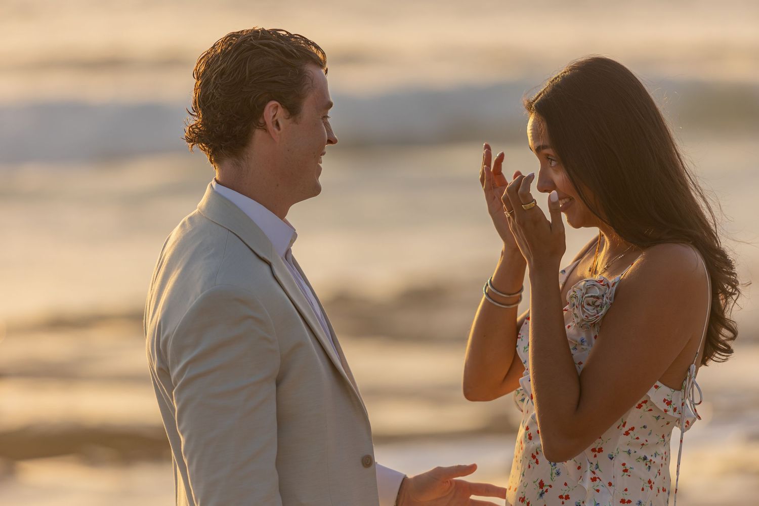 Sweet beachside engagement moment captured during sunset with ocean waves in background.