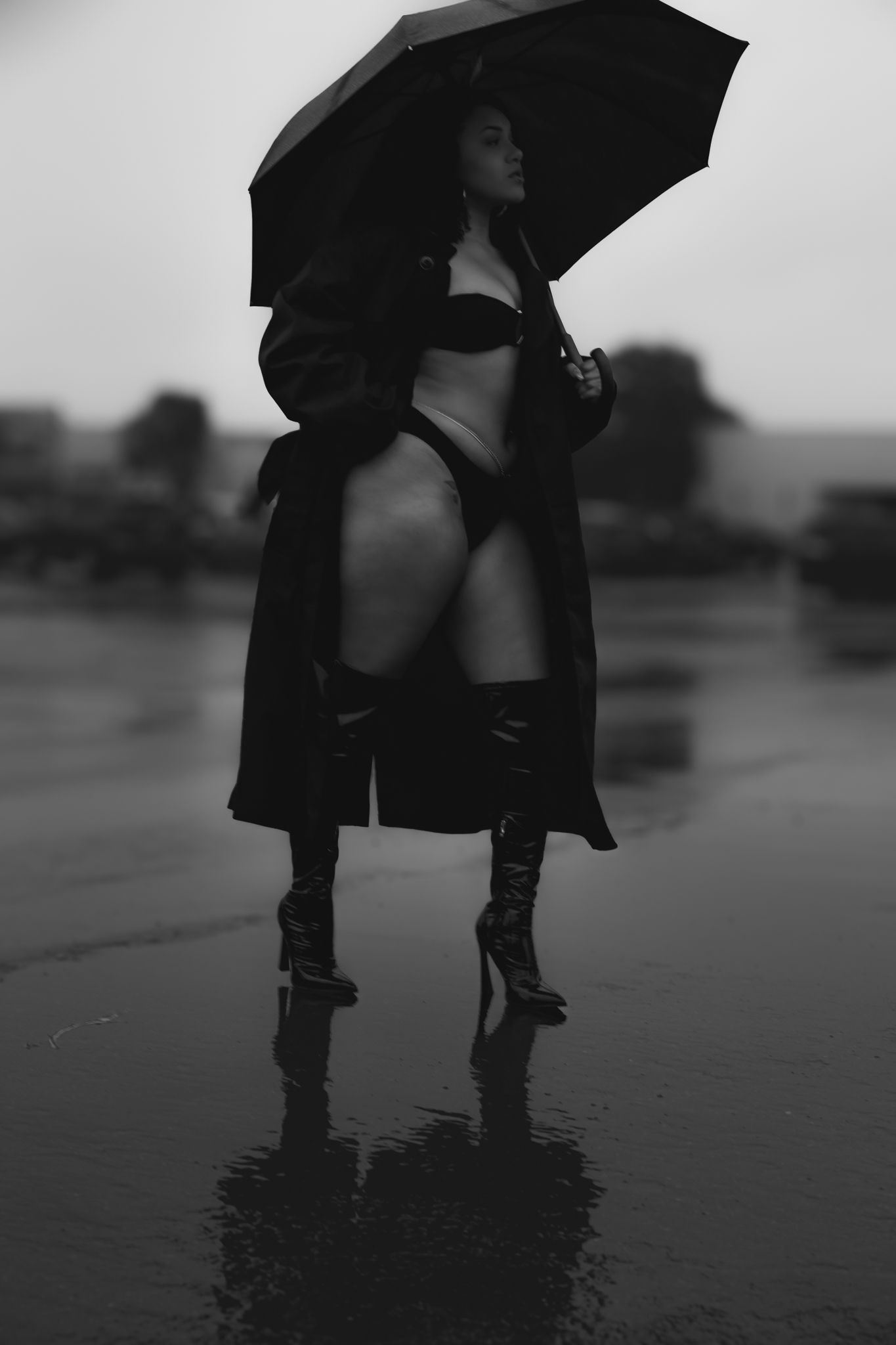 Artistic silhouette of boots and umbrella reflecting in rain puddles.