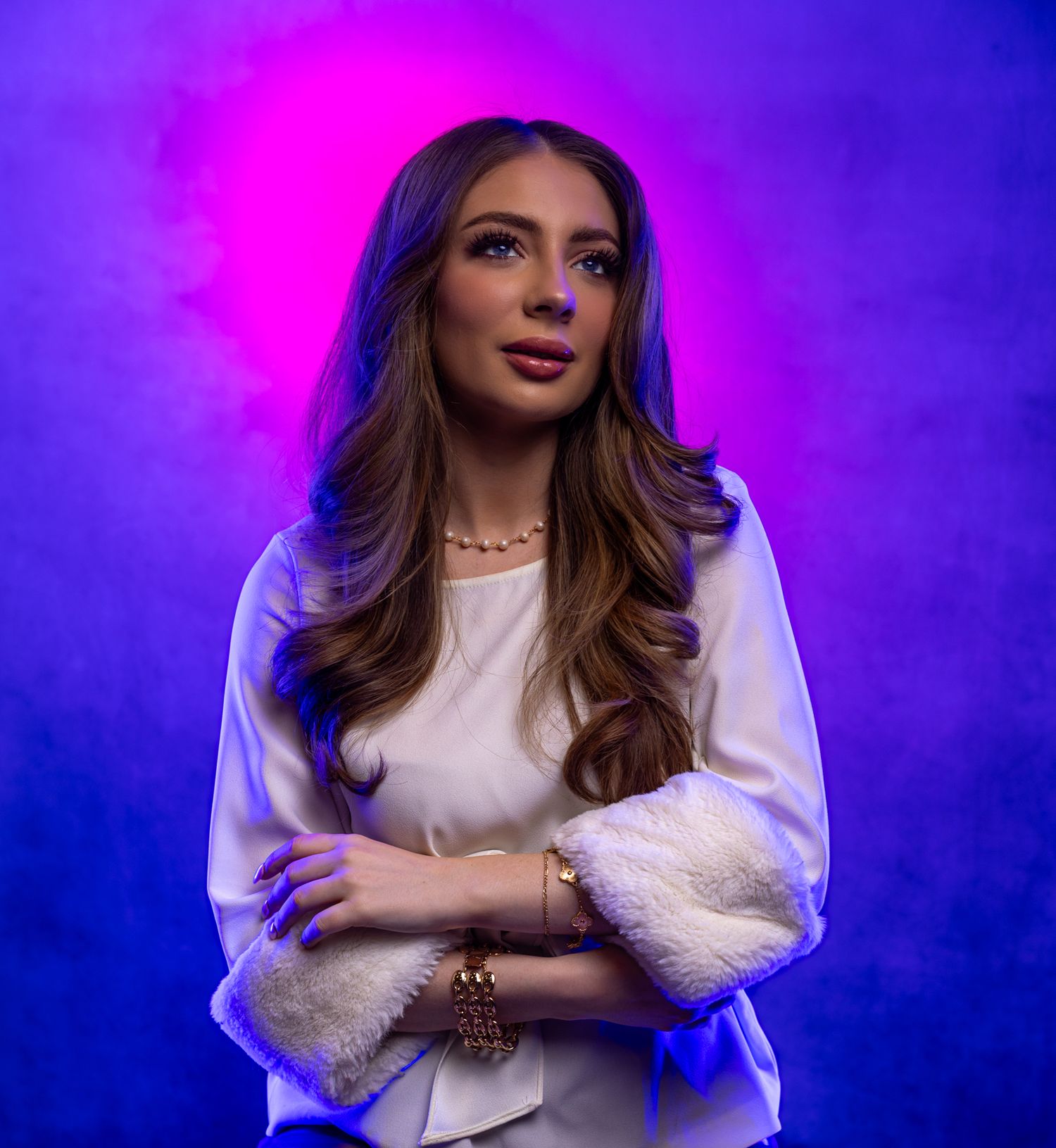 Portrait with long wavy hair in white blouse against vibrant purple and blue lighting.