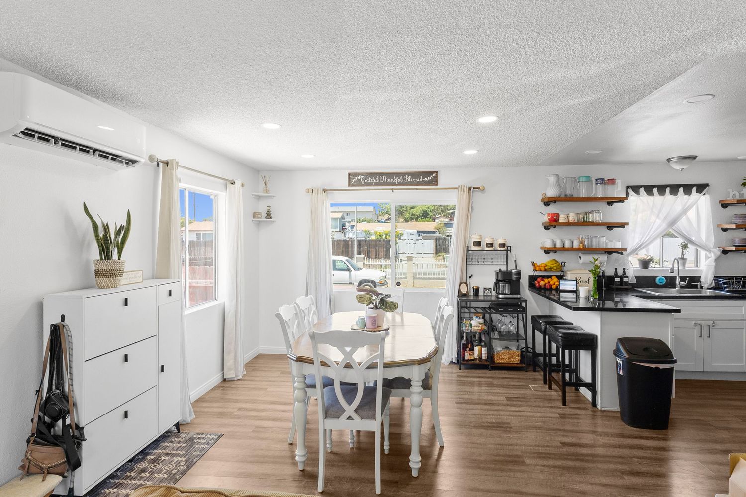 Spacious open floor plan featuring white kitchen, dining area and living room with modern decor.