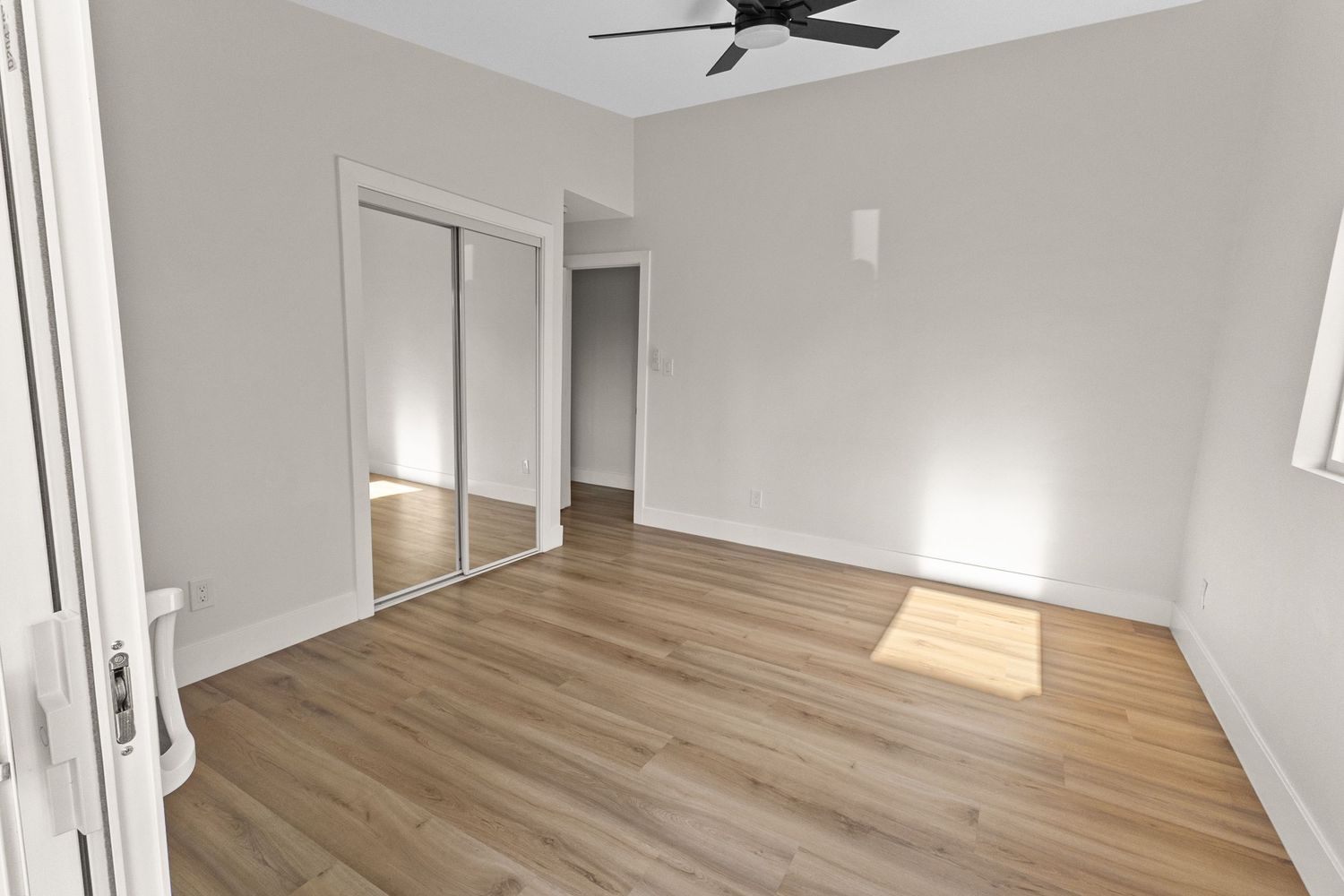Spacious unfurnished room with wooden floors and large windows letting in natural light.