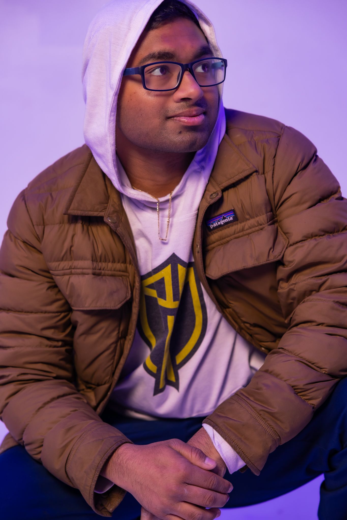 Close-up portrait in brown puffer jacket and white hoodie against purple lighting.