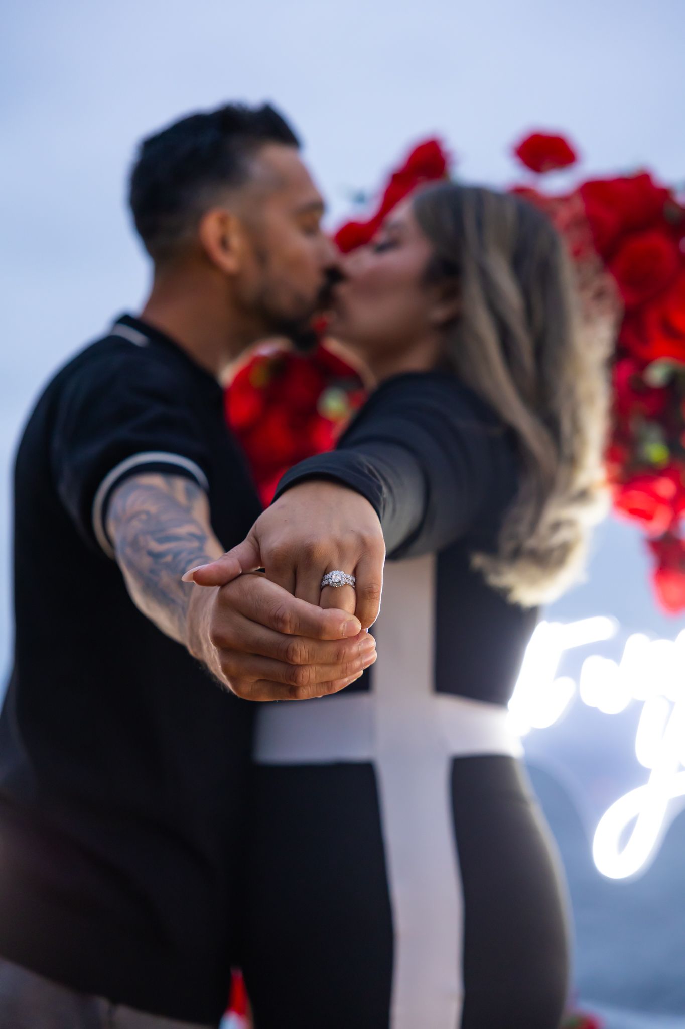 Romantic proposal scene with illuminated sign and red rose decorations.