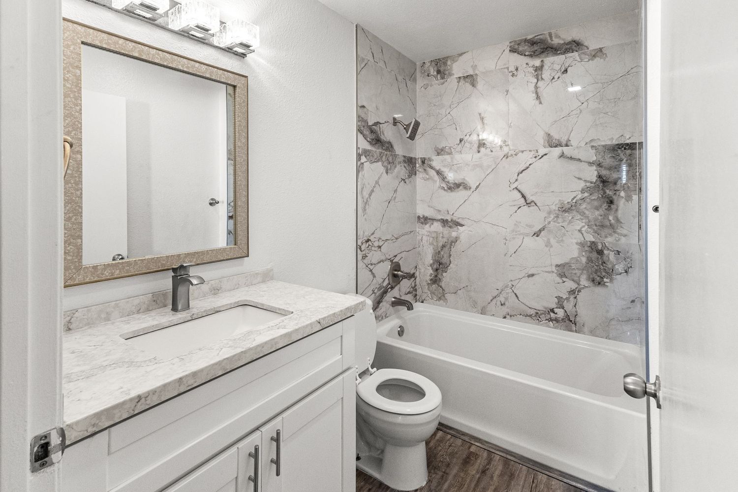 Modern bathroom with marble-look walls, framed mirror, and contemporary fixtures.