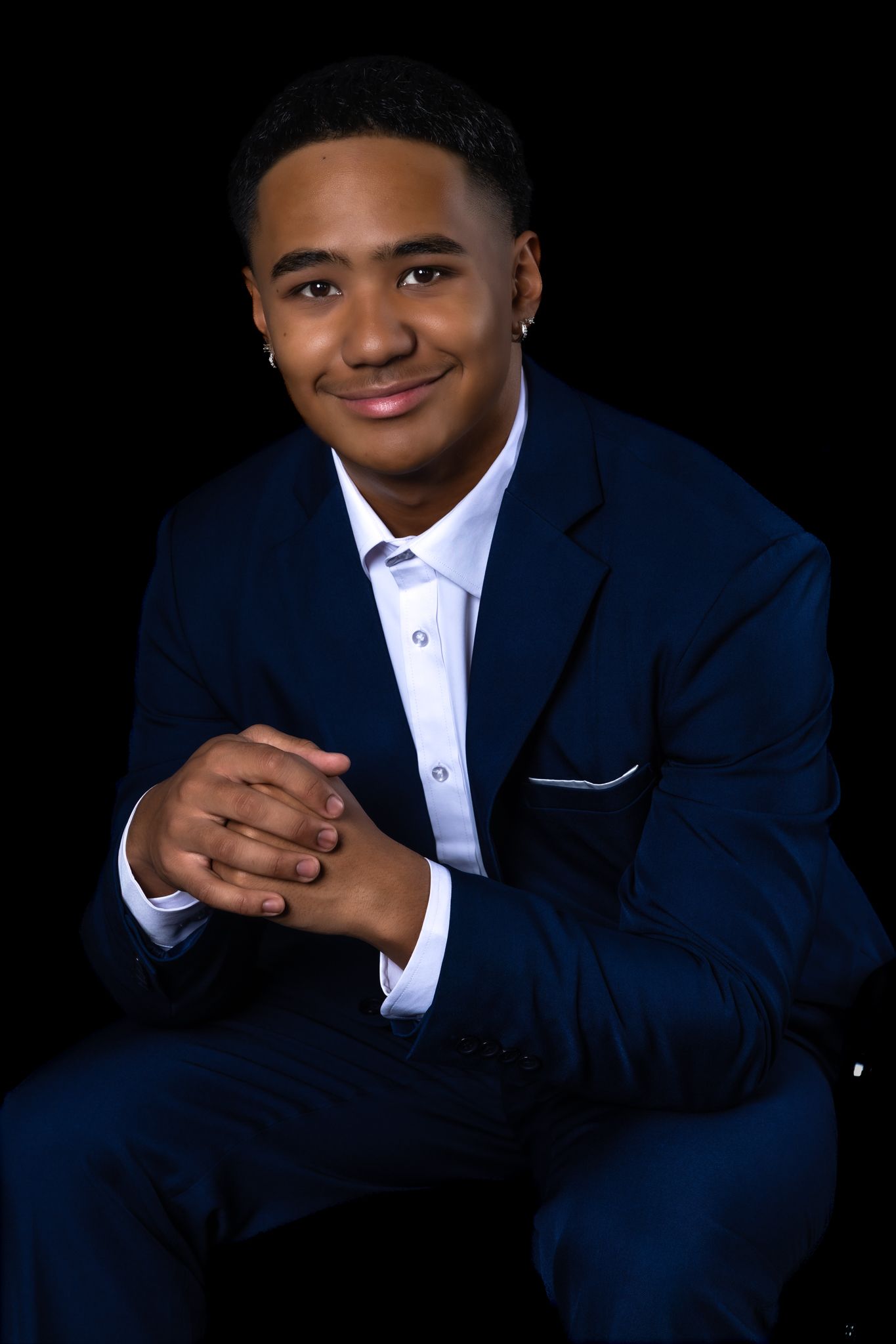 Professional studio portraits of someone wearing a navy suit and white dress shirt against a black background.