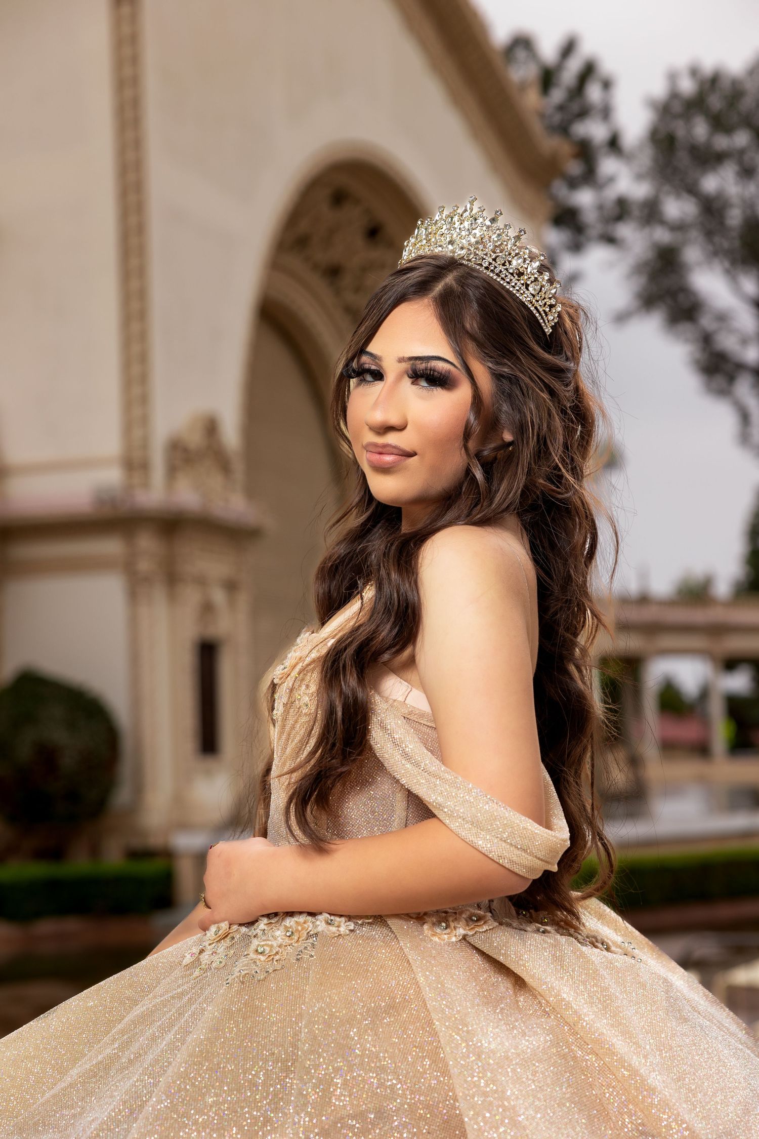 Sparkly champagne ballgown with crystal tiara photographed in an outdoor courtyard setting.