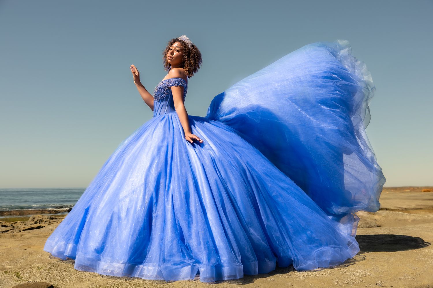 A flowing blue ballgown twirls dramatically against a sunset sky backdrop.
