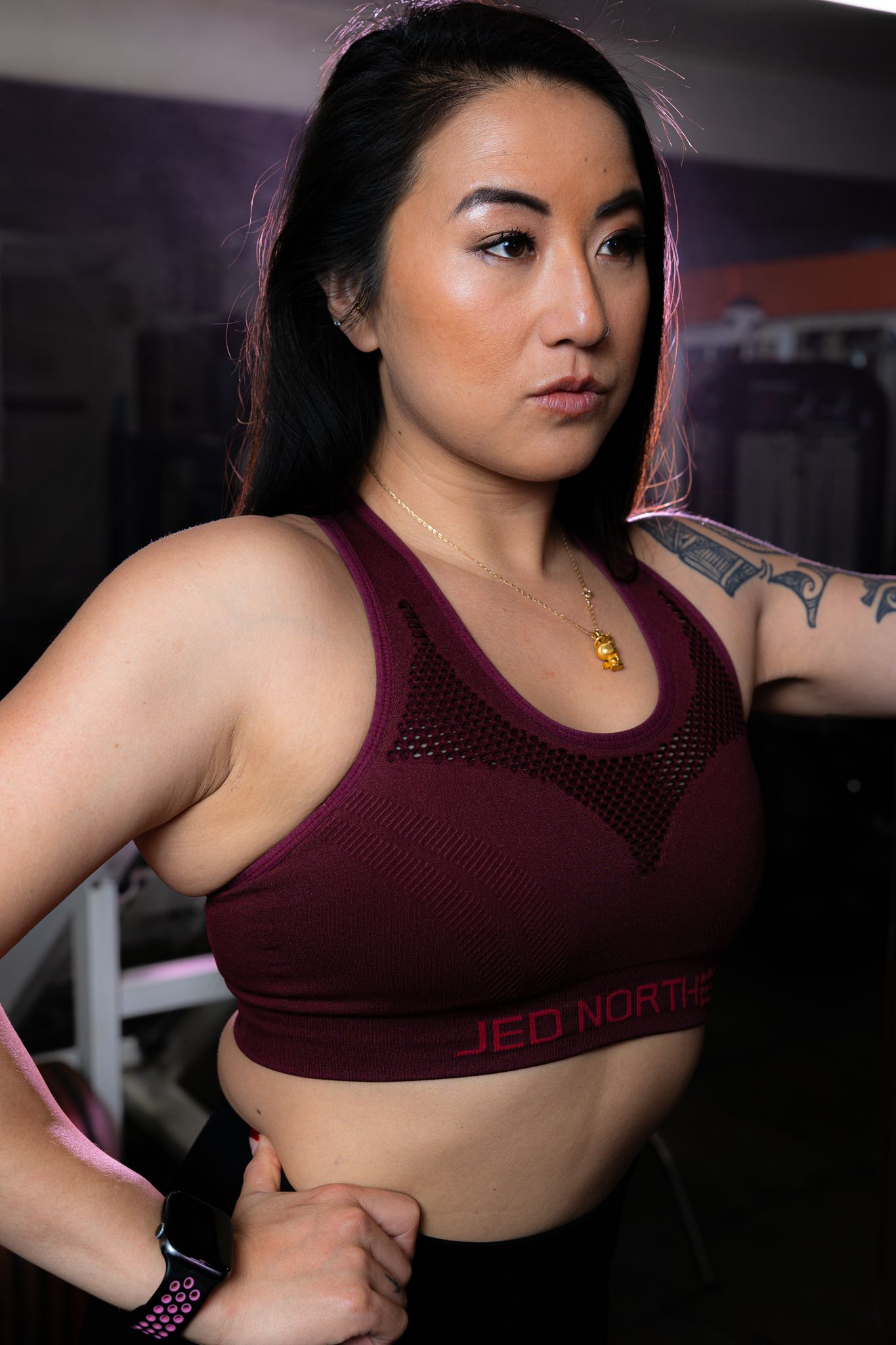 Athletic person in burgundy sports bra poses in dramatic lighting setup.