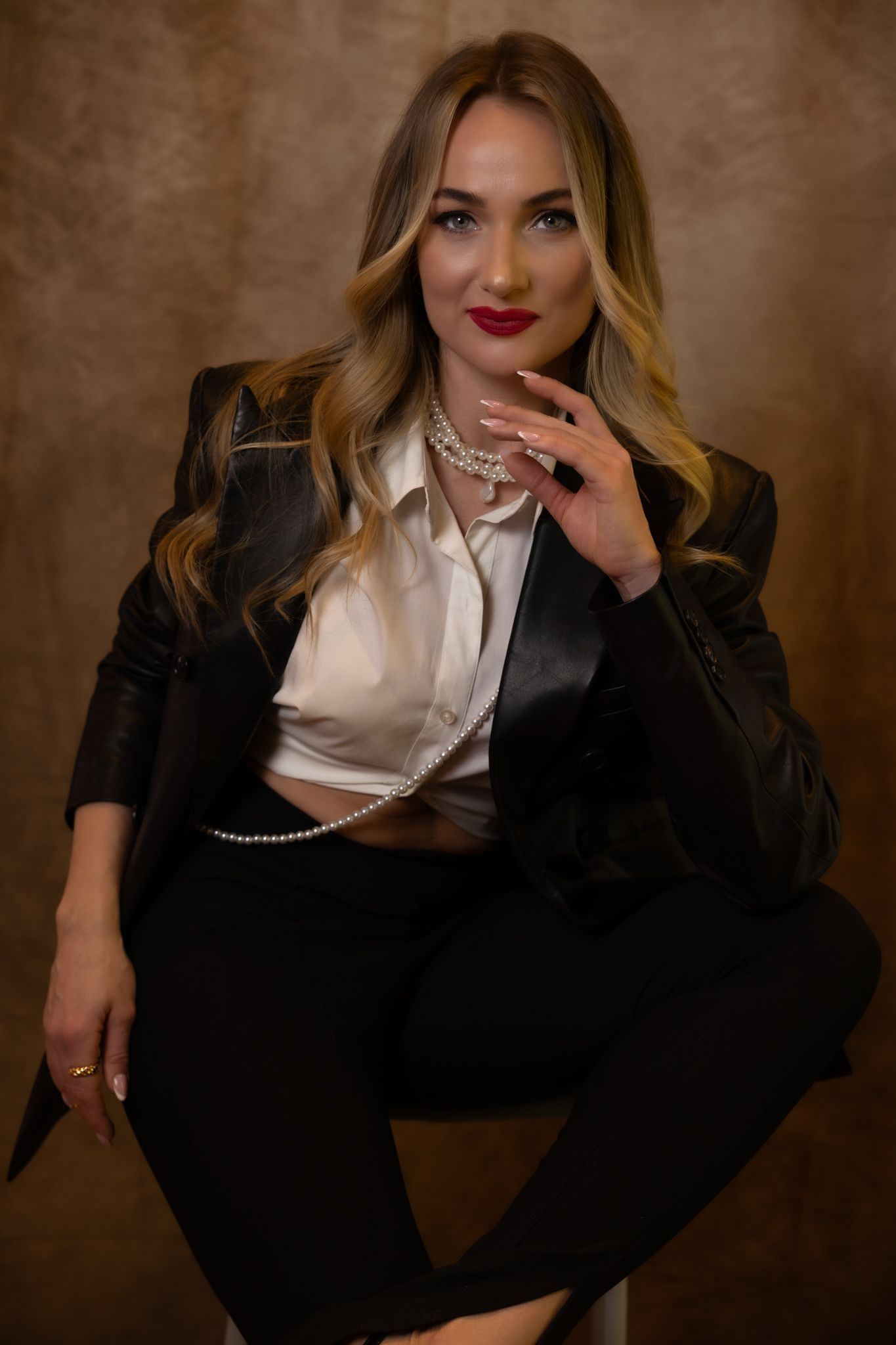 Glamorous portrait with black blazer, silk top and statement jewelry against brown backdrop.