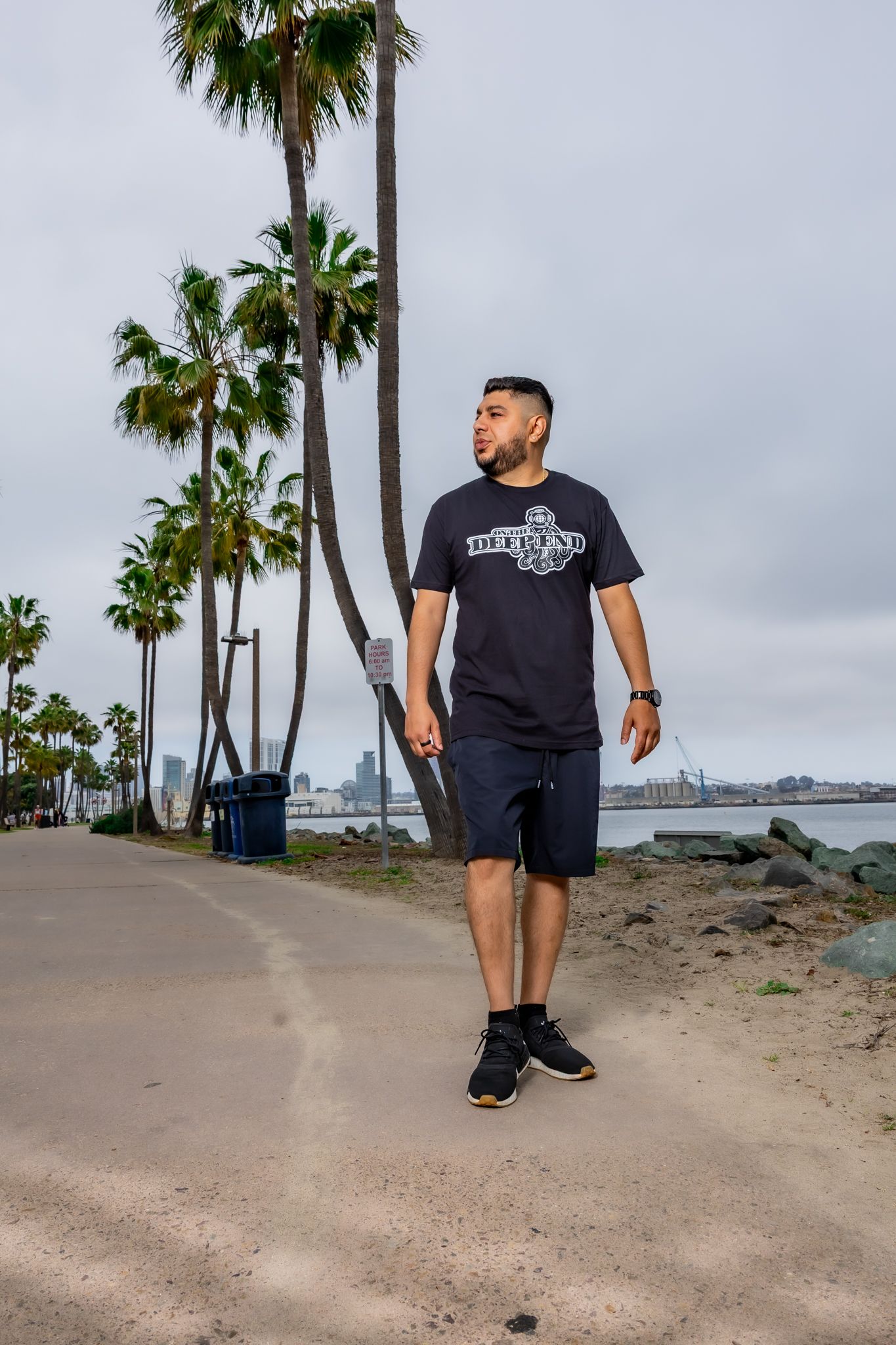 Person in black t-shirt and shorts walking on sandy beach path lined with palm trees.