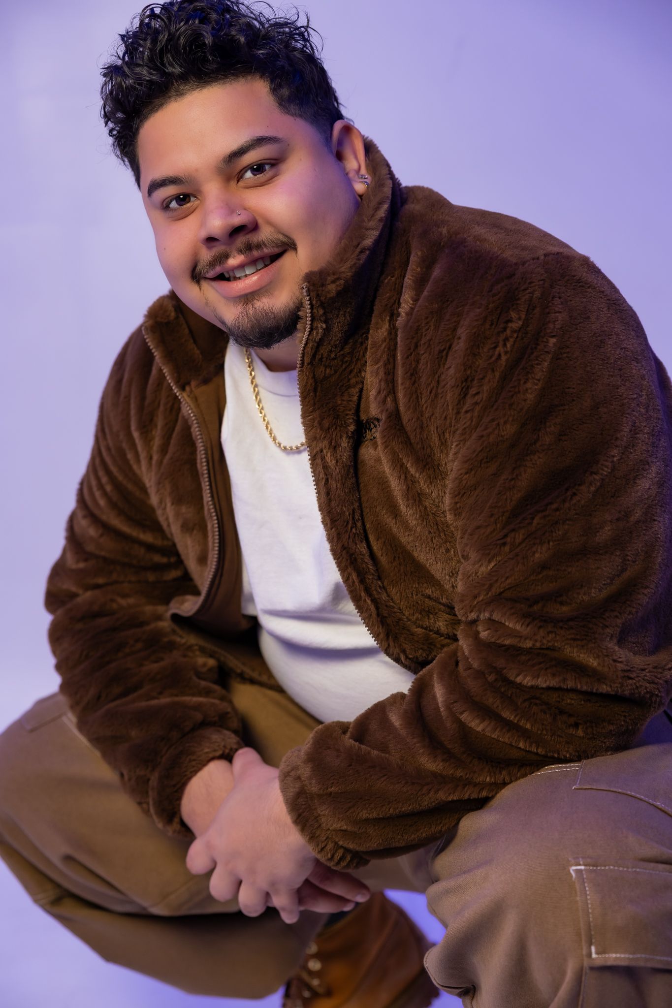 Person in corduroy jacket poses playfully against purple studio backdrop.