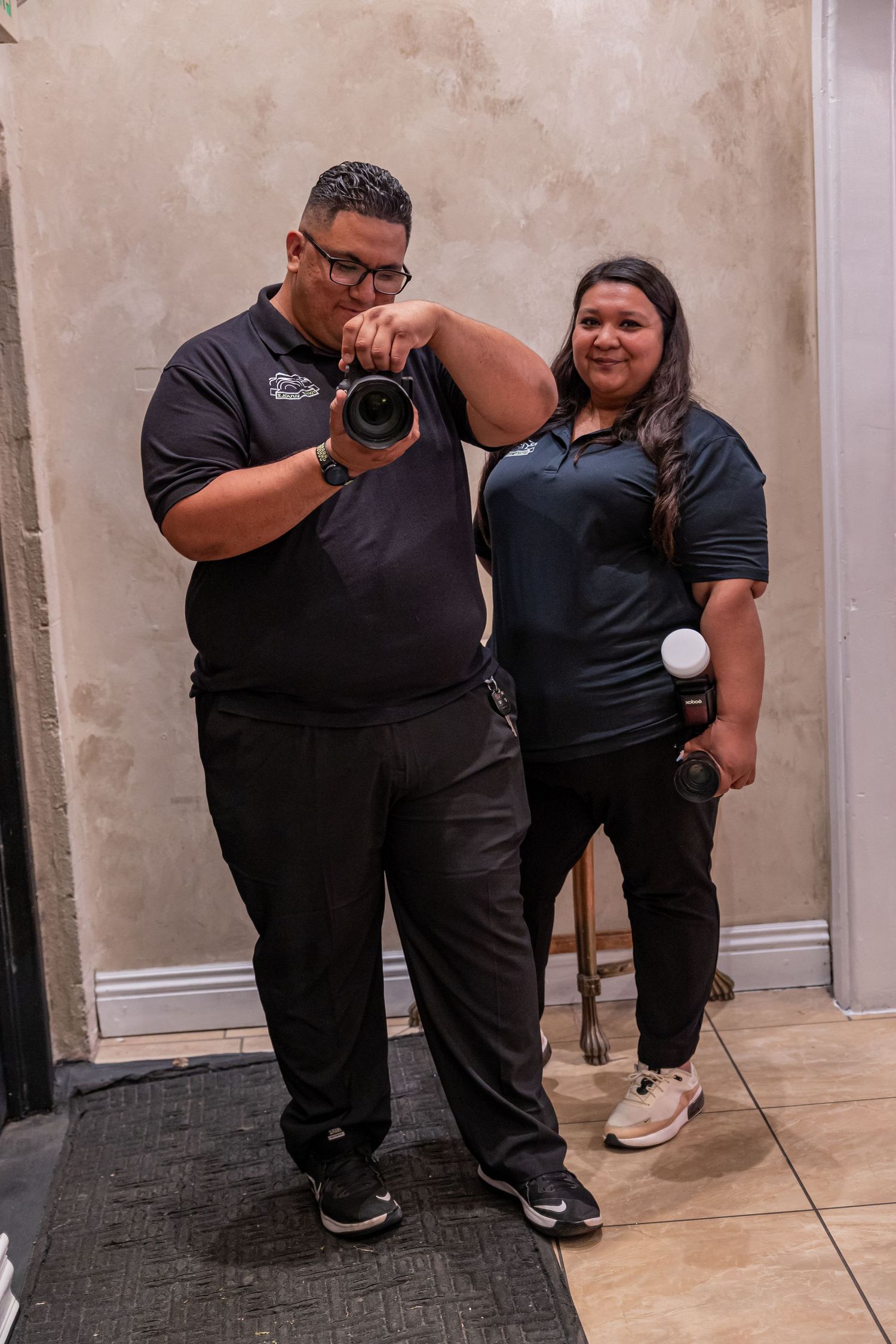 Group posing casually against a beige wall in matching black outfits on tile flooring.