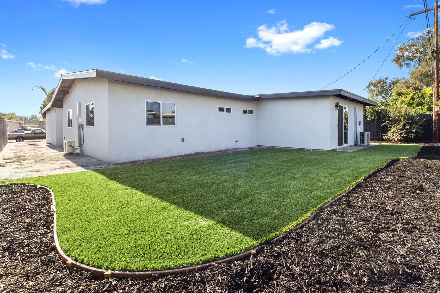 Landscaped backyard with contrasting sections of artificial turf and dark mulch under blue sky.
