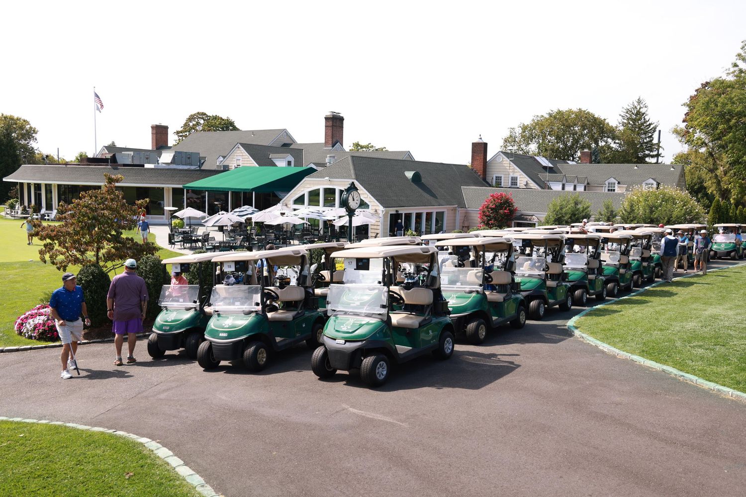 Rows of green golf carts lined up outside a classic clubhouse on a sunny day.