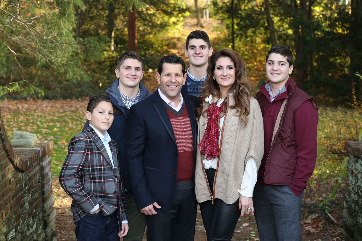 Family group poses together outdoors during autumn photoshoot with colorful fall foliage in background.