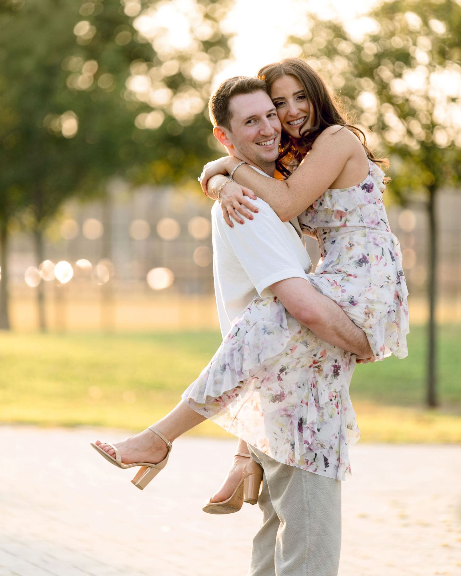 A playful engagement photo with golden sunset bokeh in a park setting.