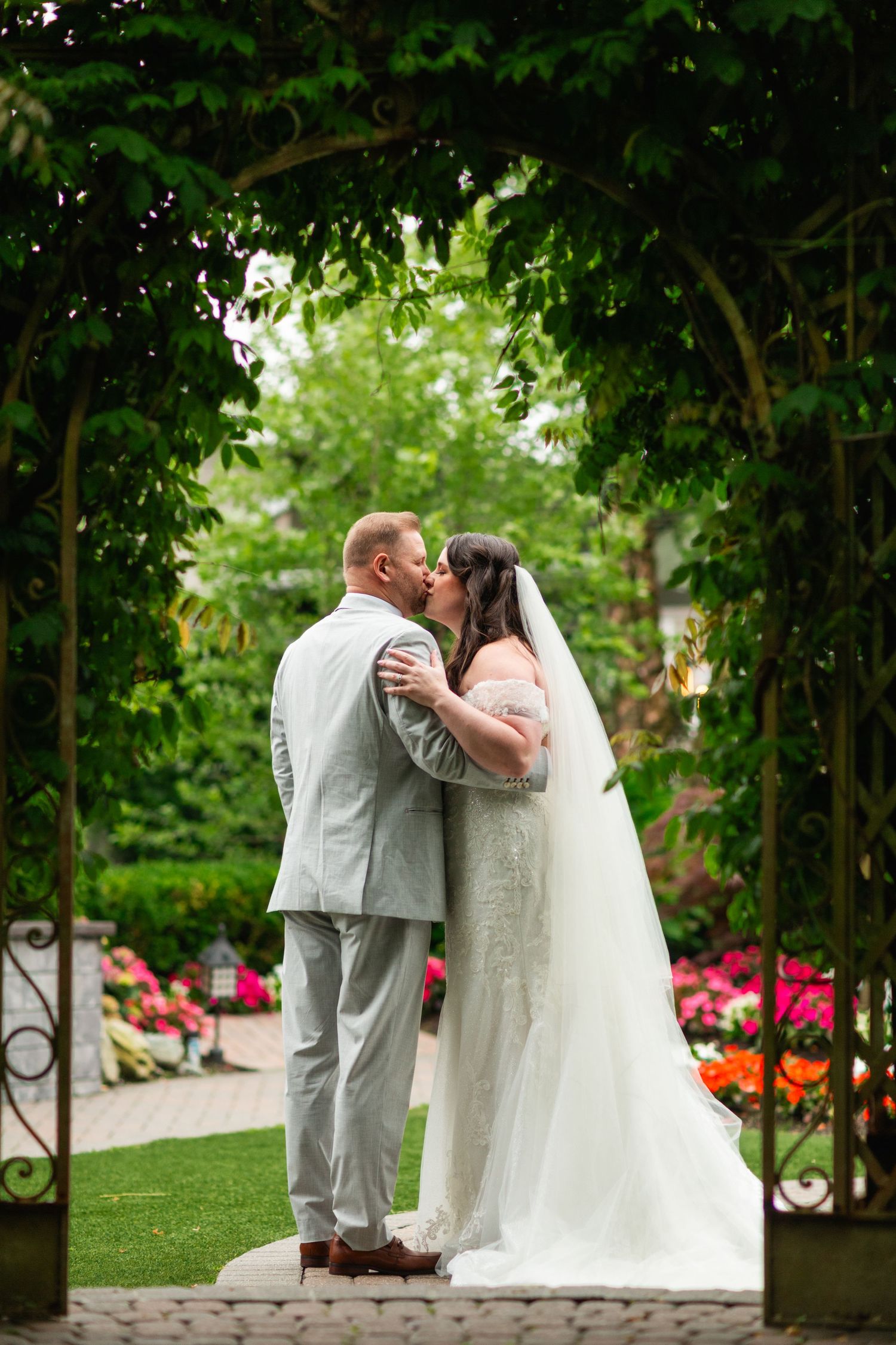 A couple shares an intimate moment in a garden setting with vibrant red flowers.