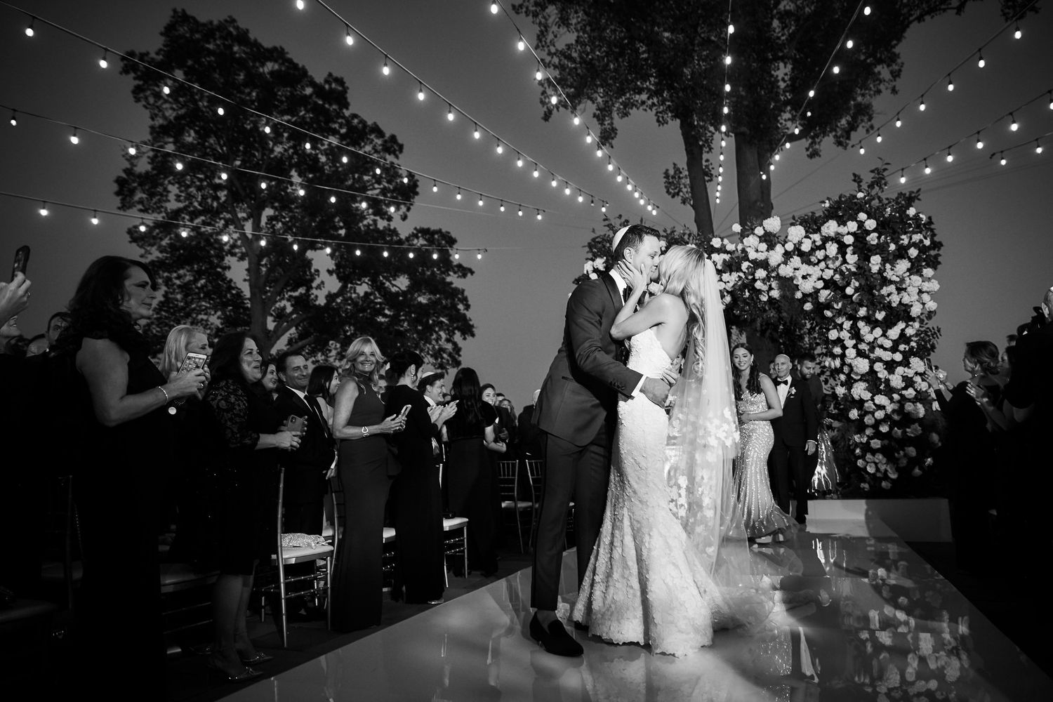 Couple shares first dance under twinkling lights at outdoor evening reception.