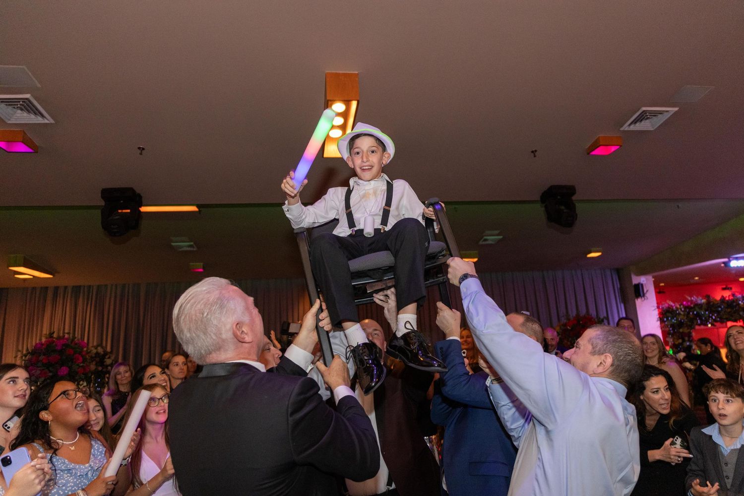 Energetic crowd dancing with raised arms under colorful party lights.