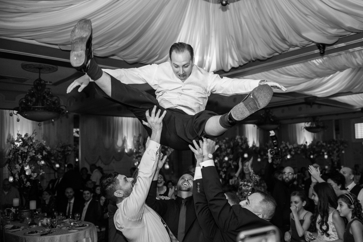Guest being lifted and carried by crowd during energetic wedding reception dance party.