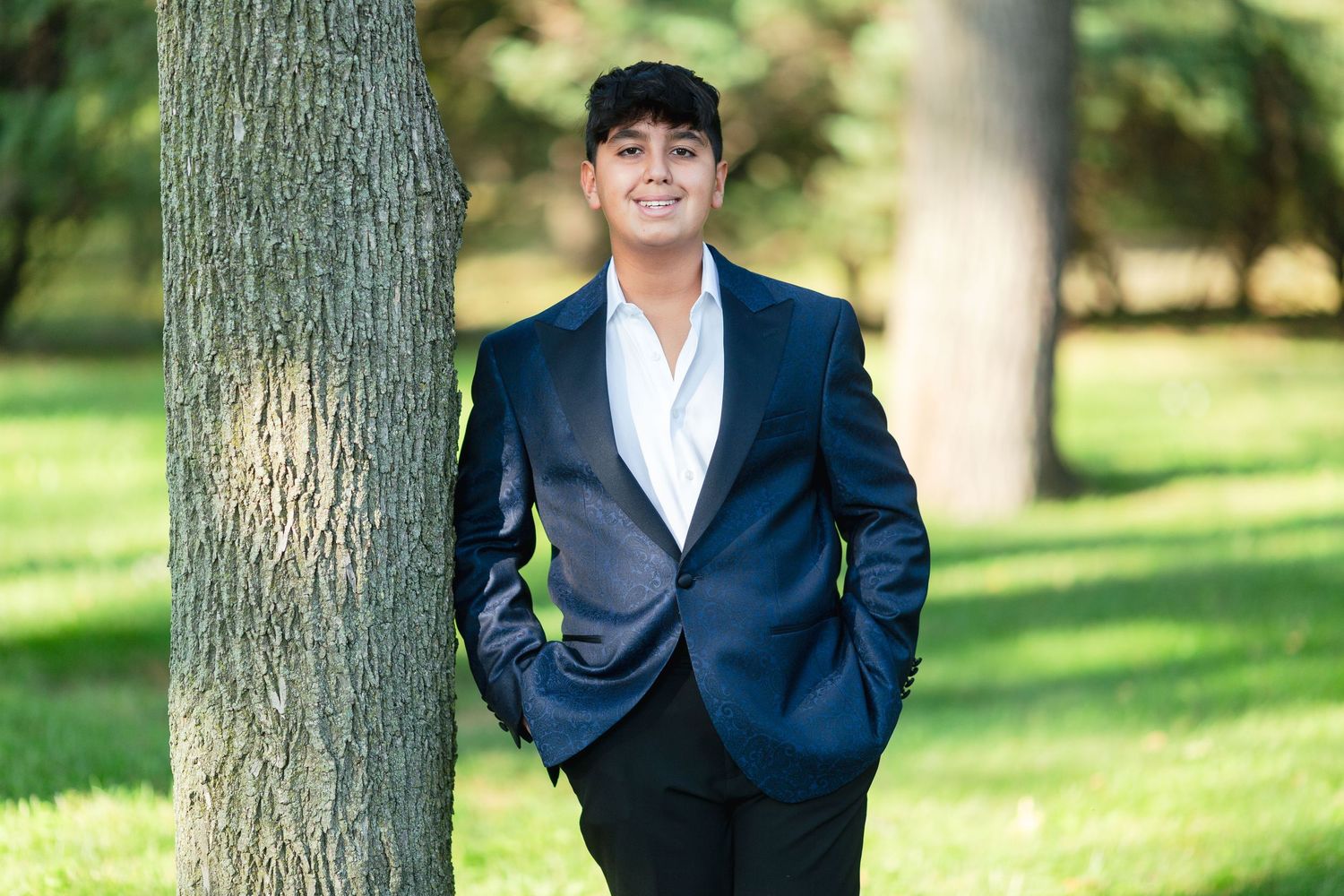 Person in navy blue suit poses against trees in outdoor portrait session.