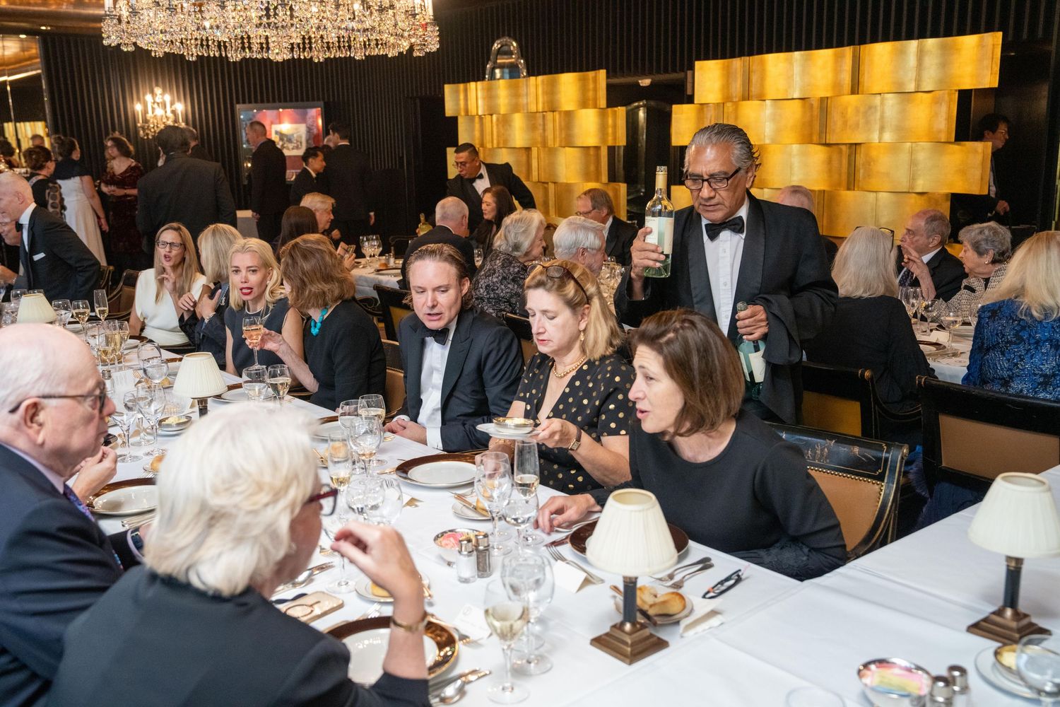 Guests enjoy a lavish formal gala dinner in a gold-accented ballroom with chandelier lighting.