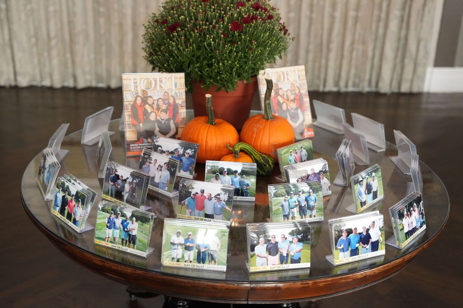 Round glass table displaying framed family photos arranged in a circle with small pumpkins and a red berry plant centerpiece.