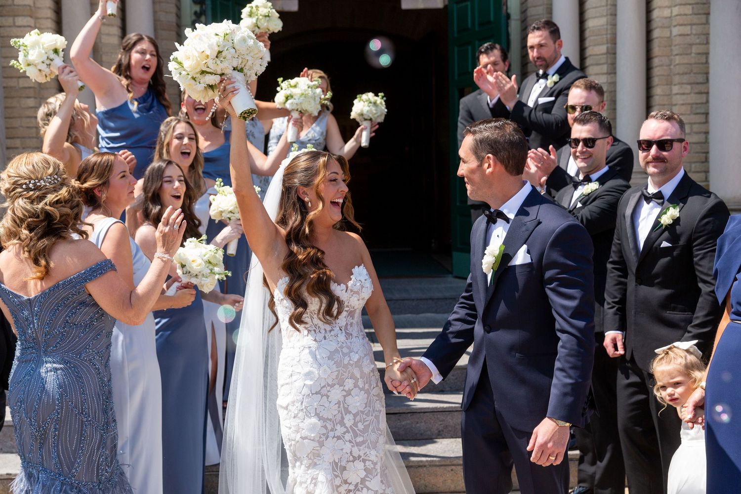 Wedding party and guests celebrating outdoors with joyful expressions and formal attire.