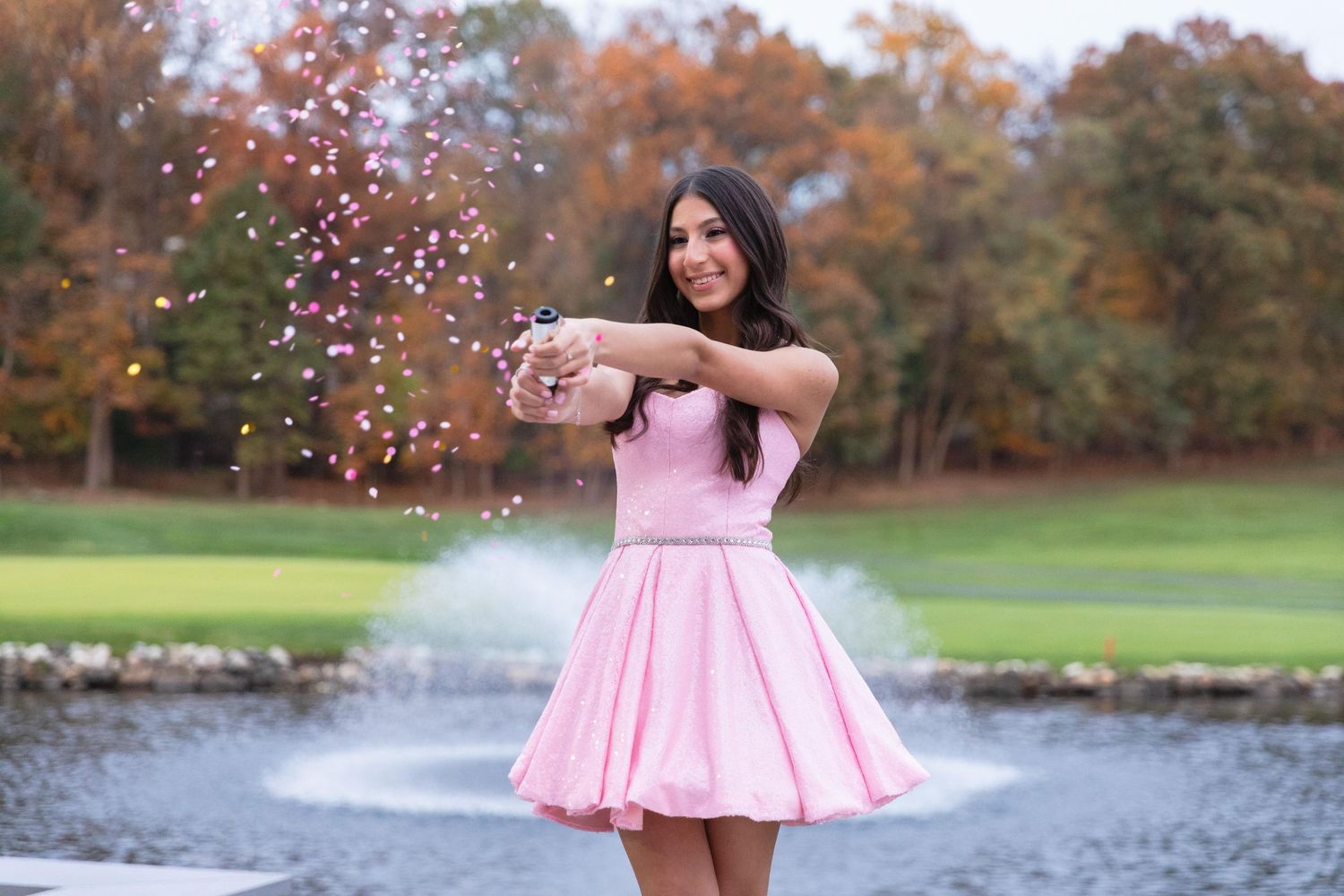 Pink dress twirling with confetti and fountain in autumn park setting.