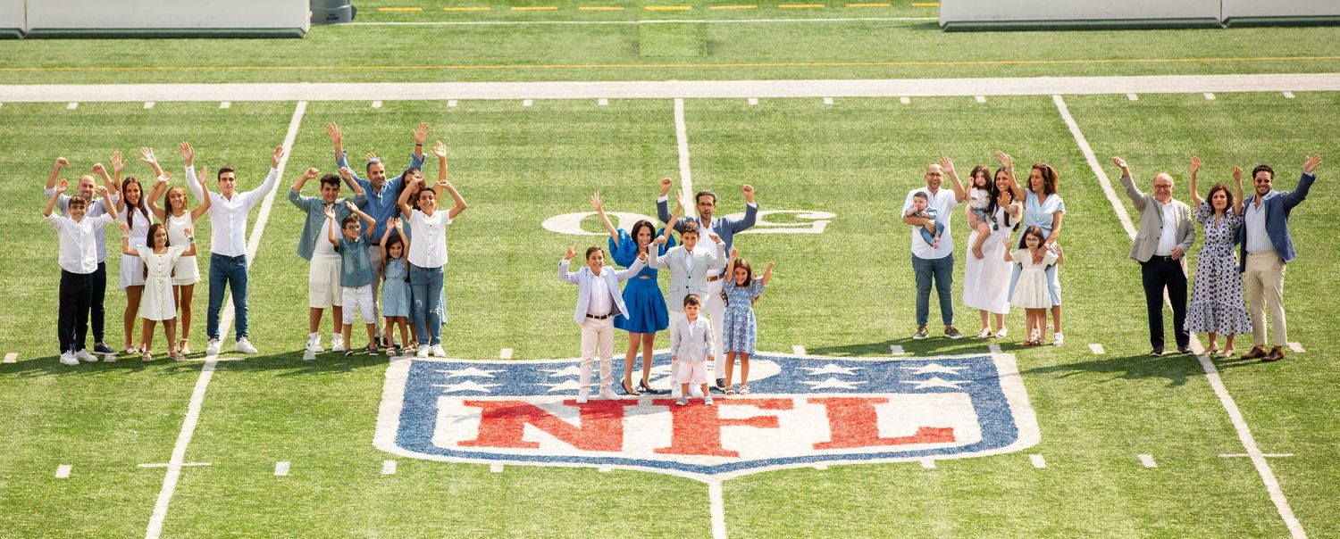 Group of people posing on NFL logo at midfield of a professional football stadium on a sunny day.