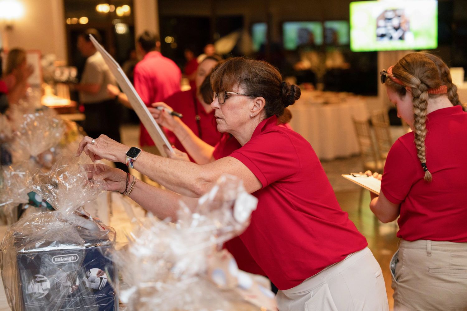 Volunteers in red polo shirts organizing silent auction items at a charity event in a banquet hall.
