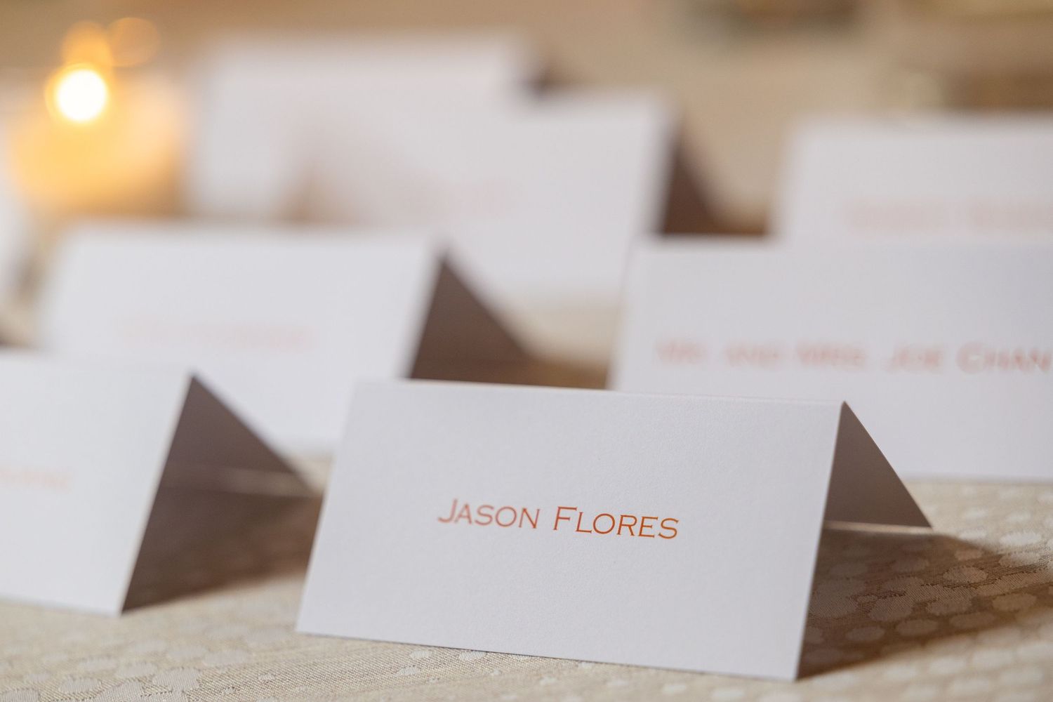 Elegant wedding place cards with red text on white folded cards, featuring Jason Flores name card in foreground.