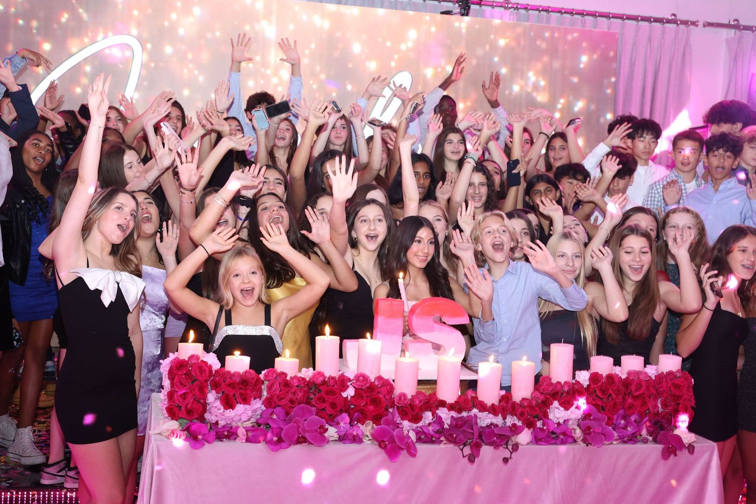 Wedding reception party with pink lighting and crowd of guests celebrating on dance floor.