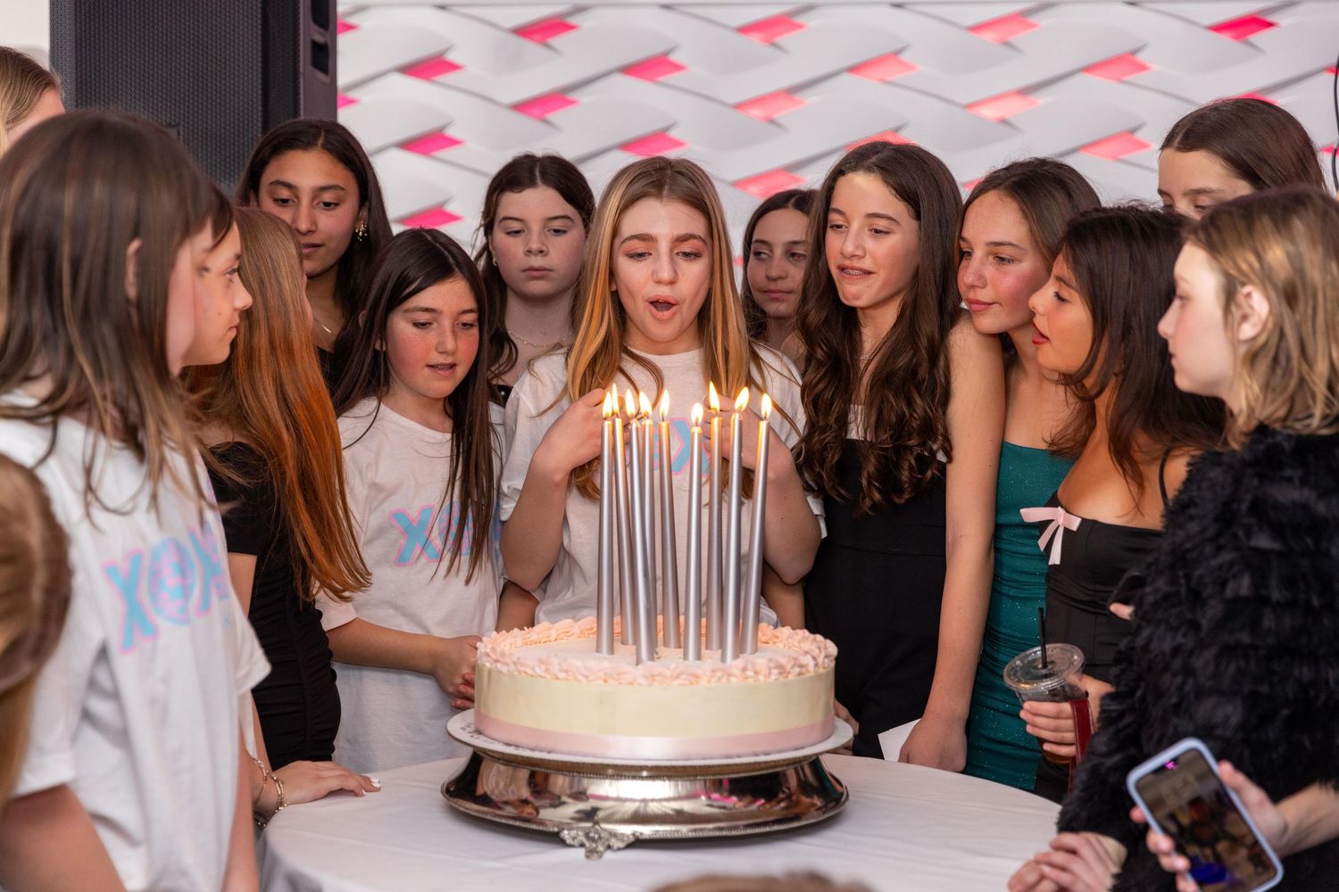 Teen girl blowing out birthday cake candles surrounded by friends at a birthday party celebration.