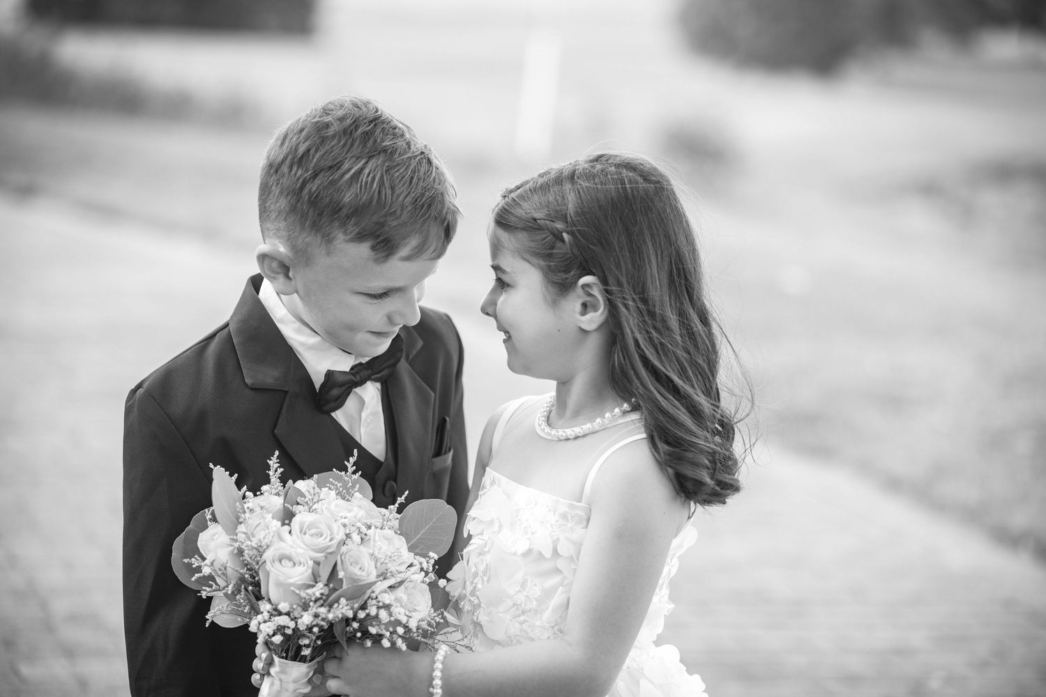 A sweet moment between young wedding attendants holding a small white bouquet.