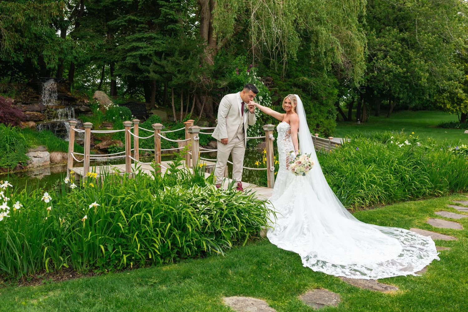 A couple in wedding attire poses together in a lush garden setting with white flowers and greenery.