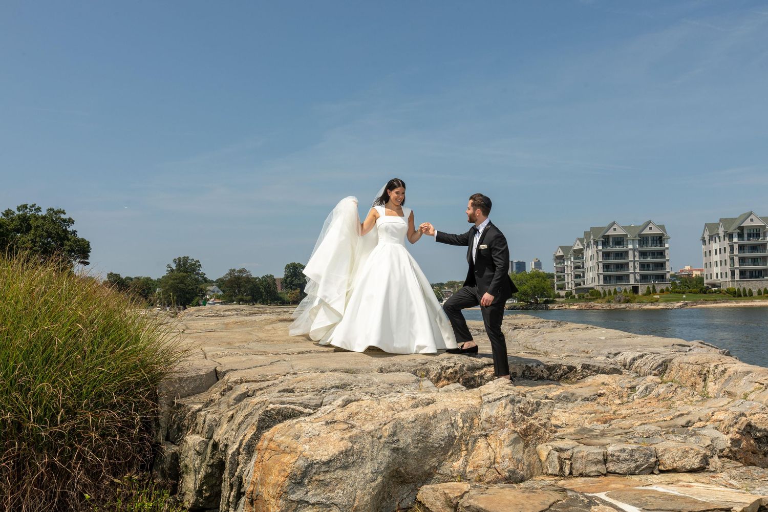 Wedding portraits captured on rocky coastal terrain with ocean and city buildings in background.
