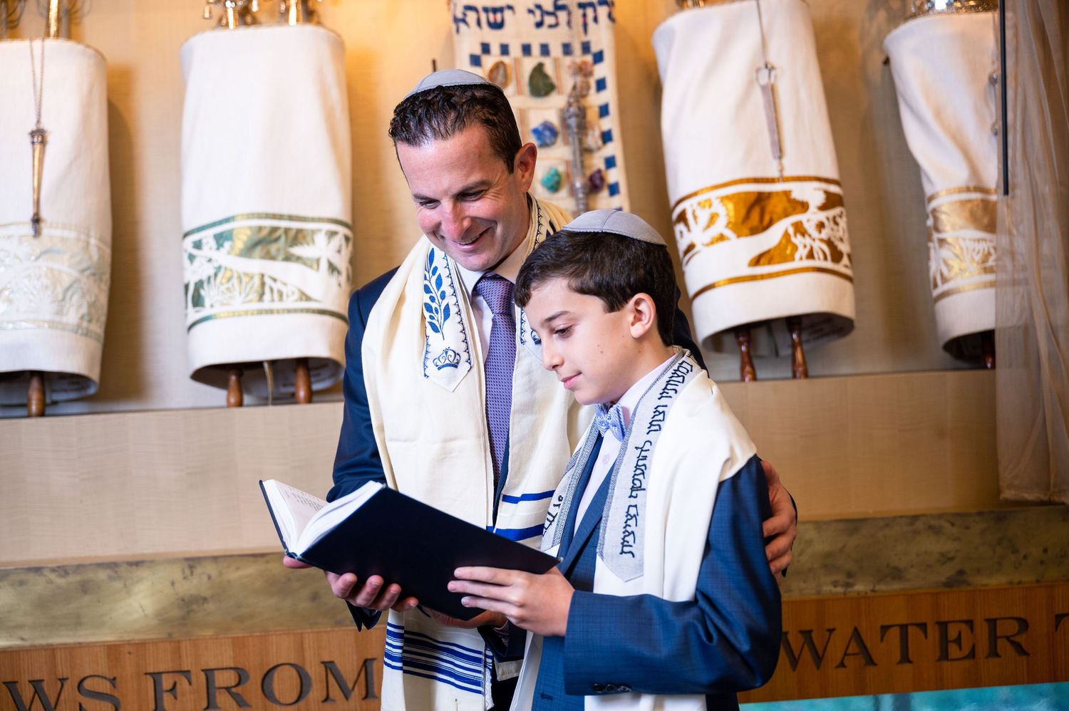 Young men in suits read from religious scrolls during a traditional bar mitzvah ceremony.