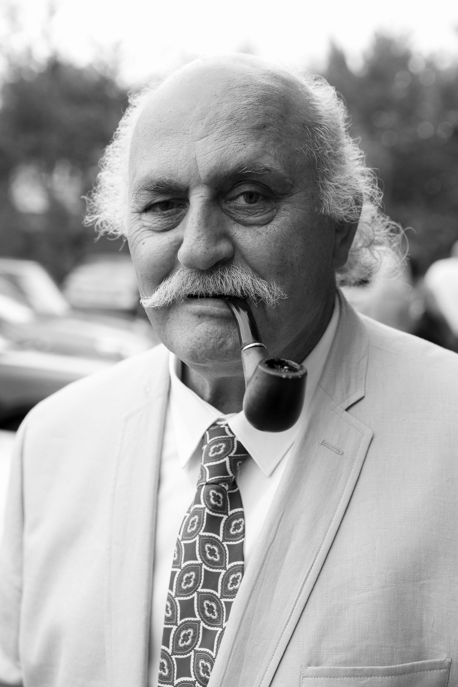A black and white portrait sequence showing someone in a white suit and patterned tie smoking a pipe.