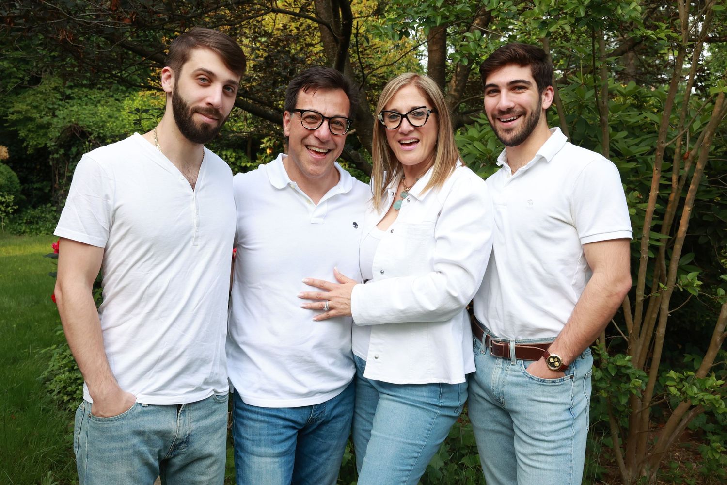Friends in coordinated white shirts and jeans pose together in a garden setting.